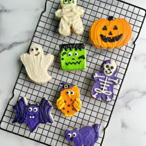 Several Halloween buttercream decorated sugar cookies on a cooling rack.