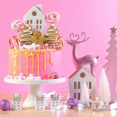 A pink backdrop with a pink Christmas candy cake and white and pink Christmas decorations for a Candyland Christmas Party theme idea..