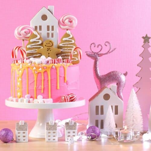 A pink backdrop with a pink Christmas candy cake and white and pink Christmas decorations for a Candyland Christmas Party theme idea..