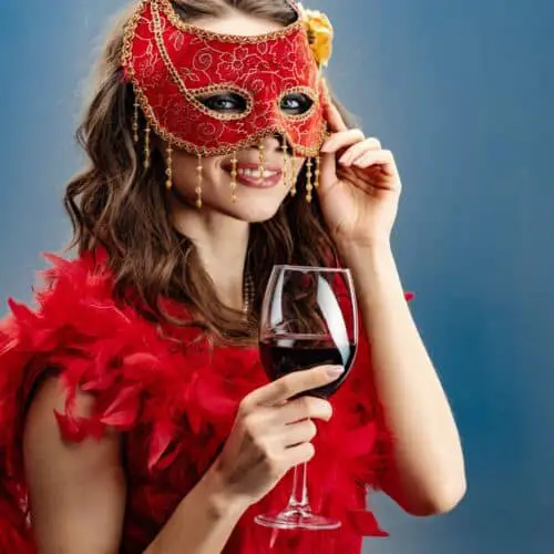 A woman in a red costume with a red feather boa, a red mask and a glass of wine at a themed Christmas Party.