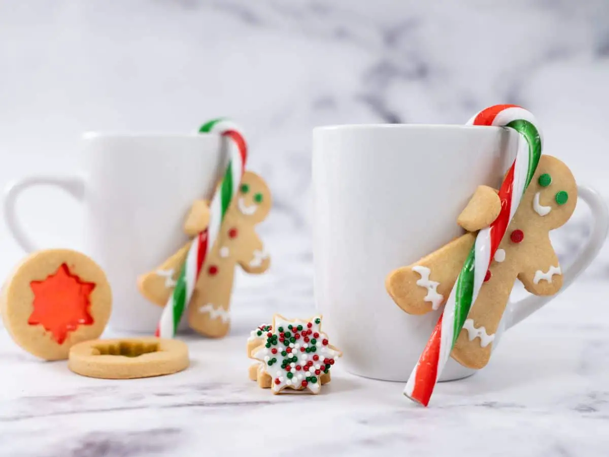 Gingerbread men with a candy cane attached to coffee mugs to decorate a Christmas table.