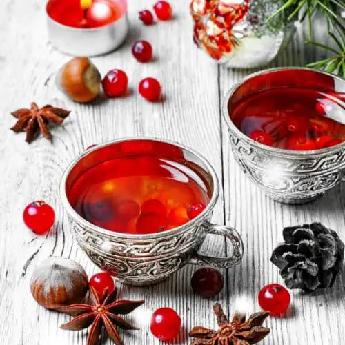 A Christmas tea party themed table with silver mugs full of hot red tea with berries and greenery.