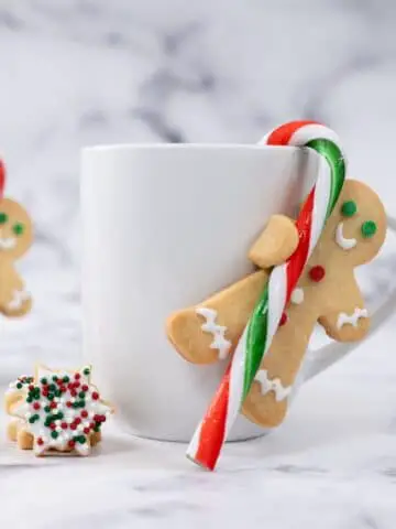 Gingerbread men with a candy cane attached to coffee mugs for a Candyland Christmas Party Theme.