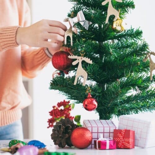 A woman's hands decorating a mini Christmas tree with ornaments.