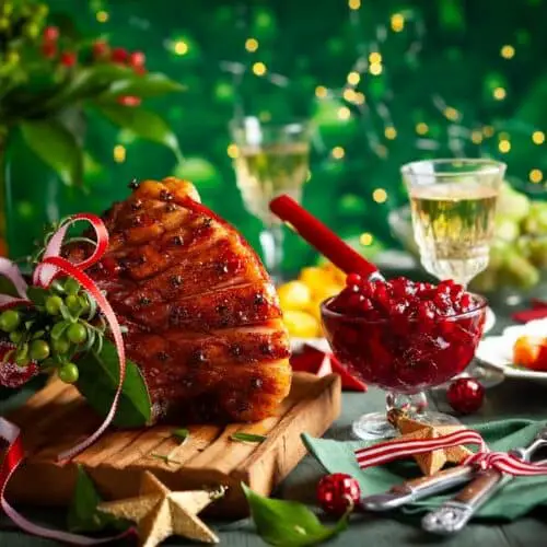 A table of food with ham, cranberry sauce, and holiday decor in the background.