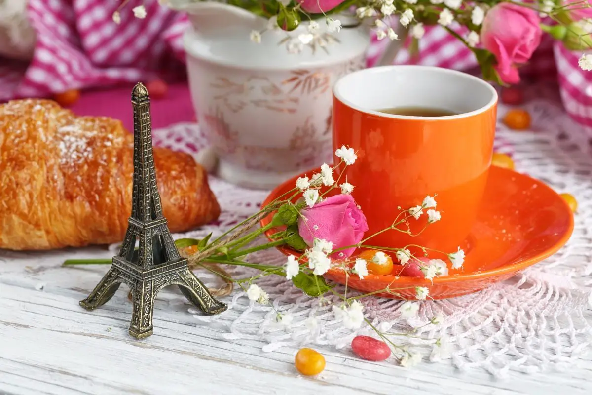 A cup of coffee, a croissant, and a mini eiffel tower on a French themed tablescape.