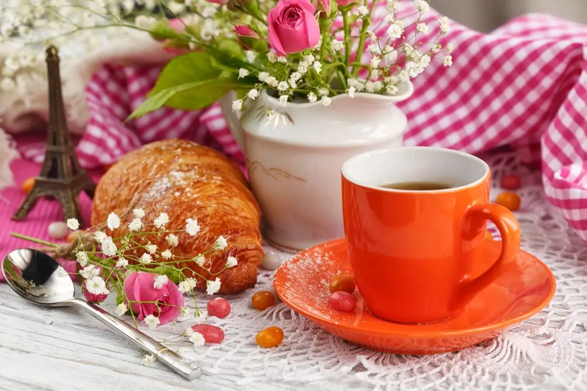 A cup of coffee, a croissant, and a mini eiffel tower at a Paris themed party.