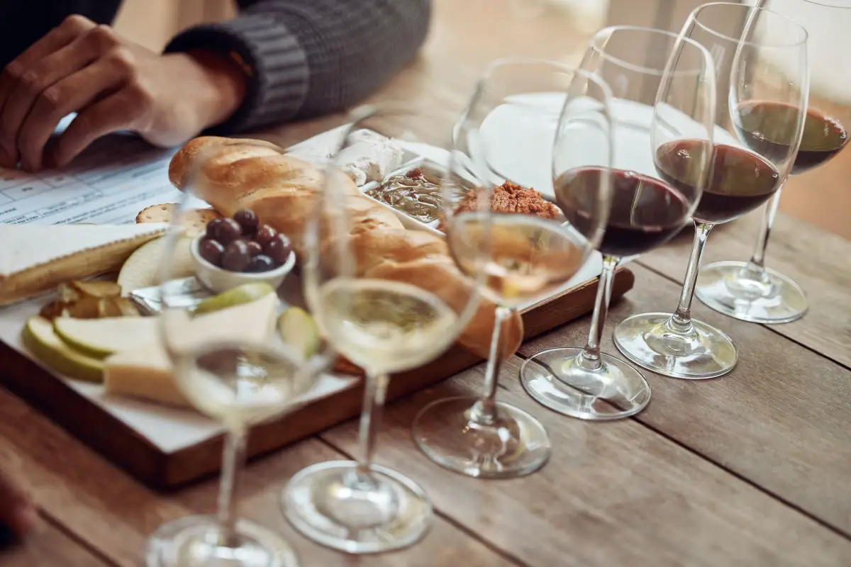 A wine flight in several wine glasses in front of a French fruit and cheese board.