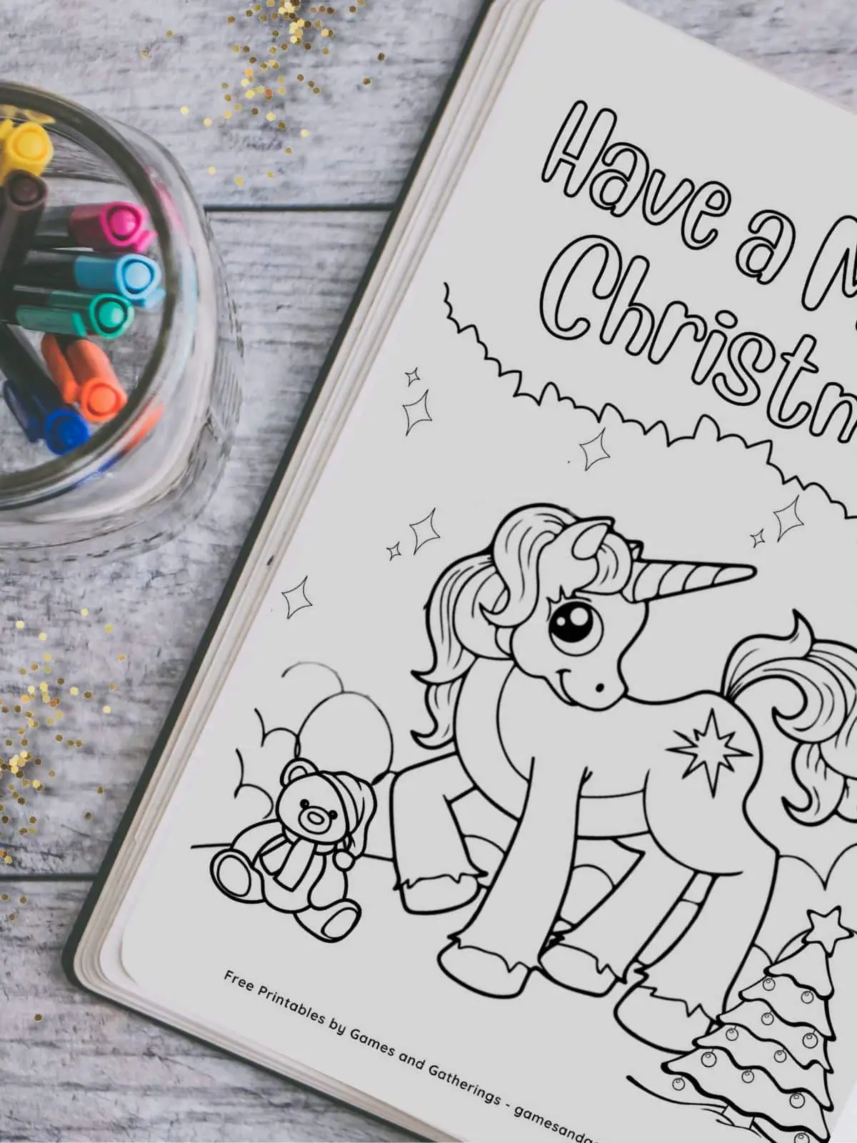 A christmas unicorn coloring book on a table with some colorful markers and gold glitter.
