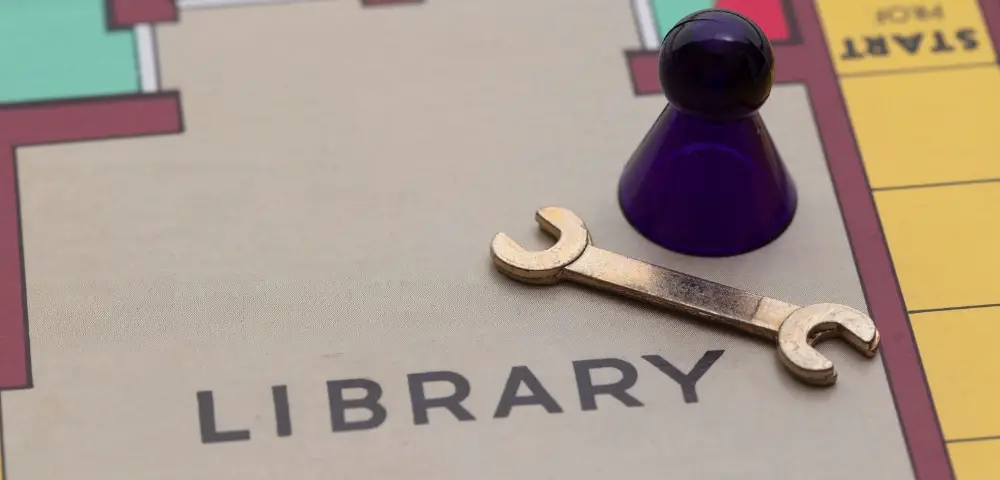 A closeup of the mystery board game clue or cluedo showing the words "library" and a wrench prop.