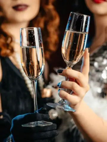 Two women cheers-ing with champagne glasses at a Great Gatsby party.