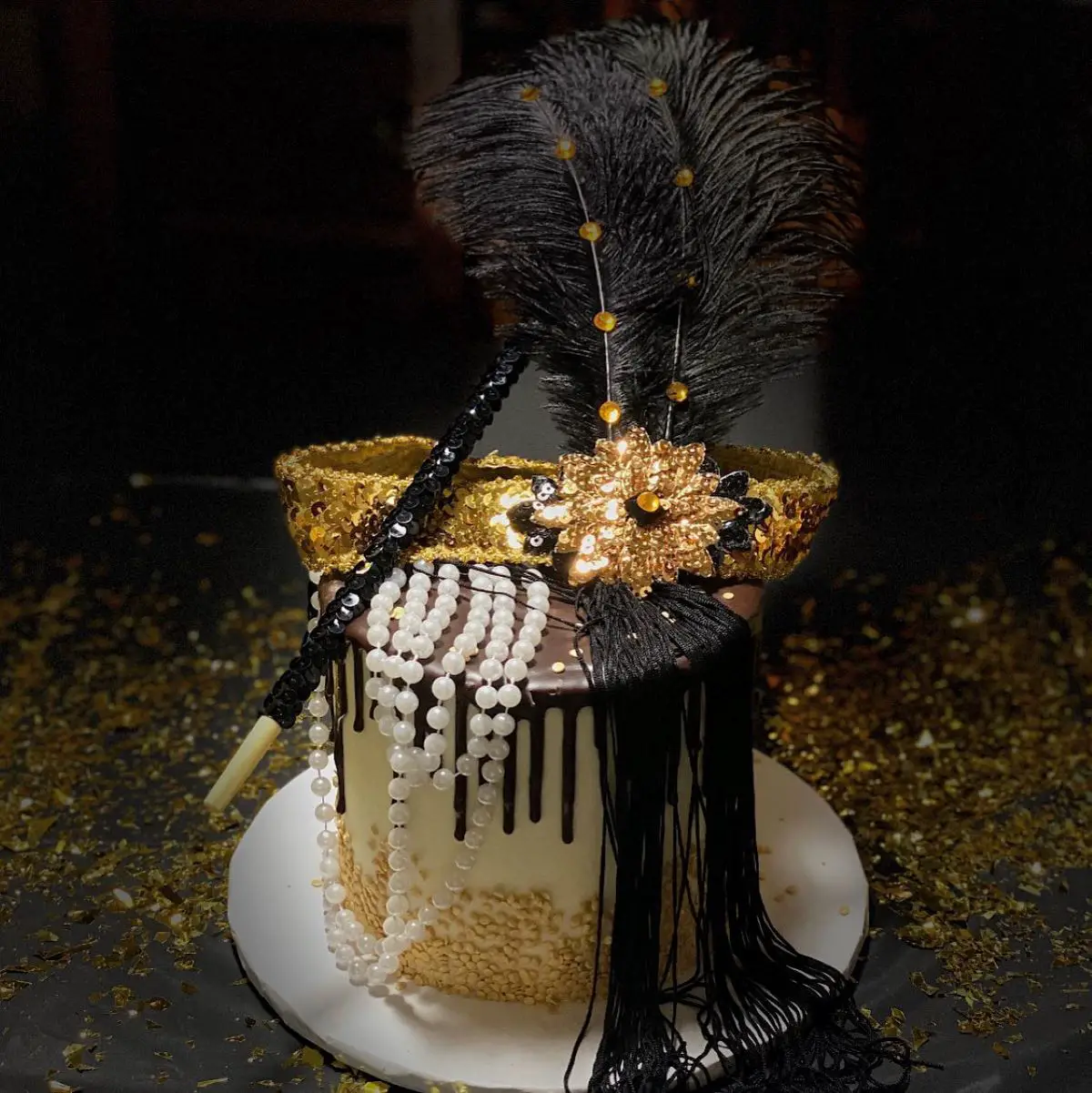 A Great Gatsby cake decorated with featherss and pearls.