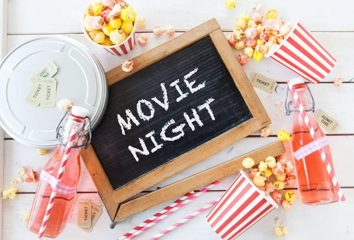 A chalkboard that says "movie night" with striped movie-themed straws and cups with popcorn.