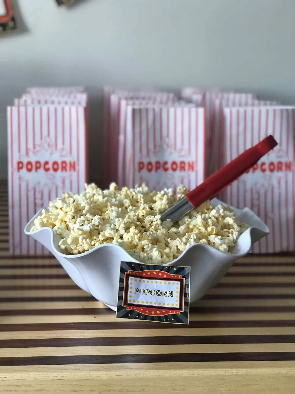 A bowl of movie popcorn with movie theater popcorn bags behind it.