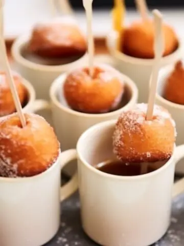 White mini coffee mugs with a skewer with a donut hole on it.